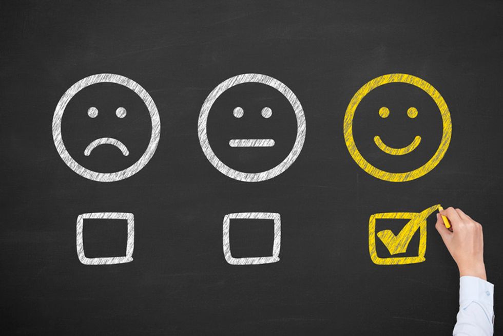 three chalk drawn simple faces, one is white and sad, the next is white and neutral, and the final face is smiling and yellow, each has a check box below it but only the yellow box is checked.